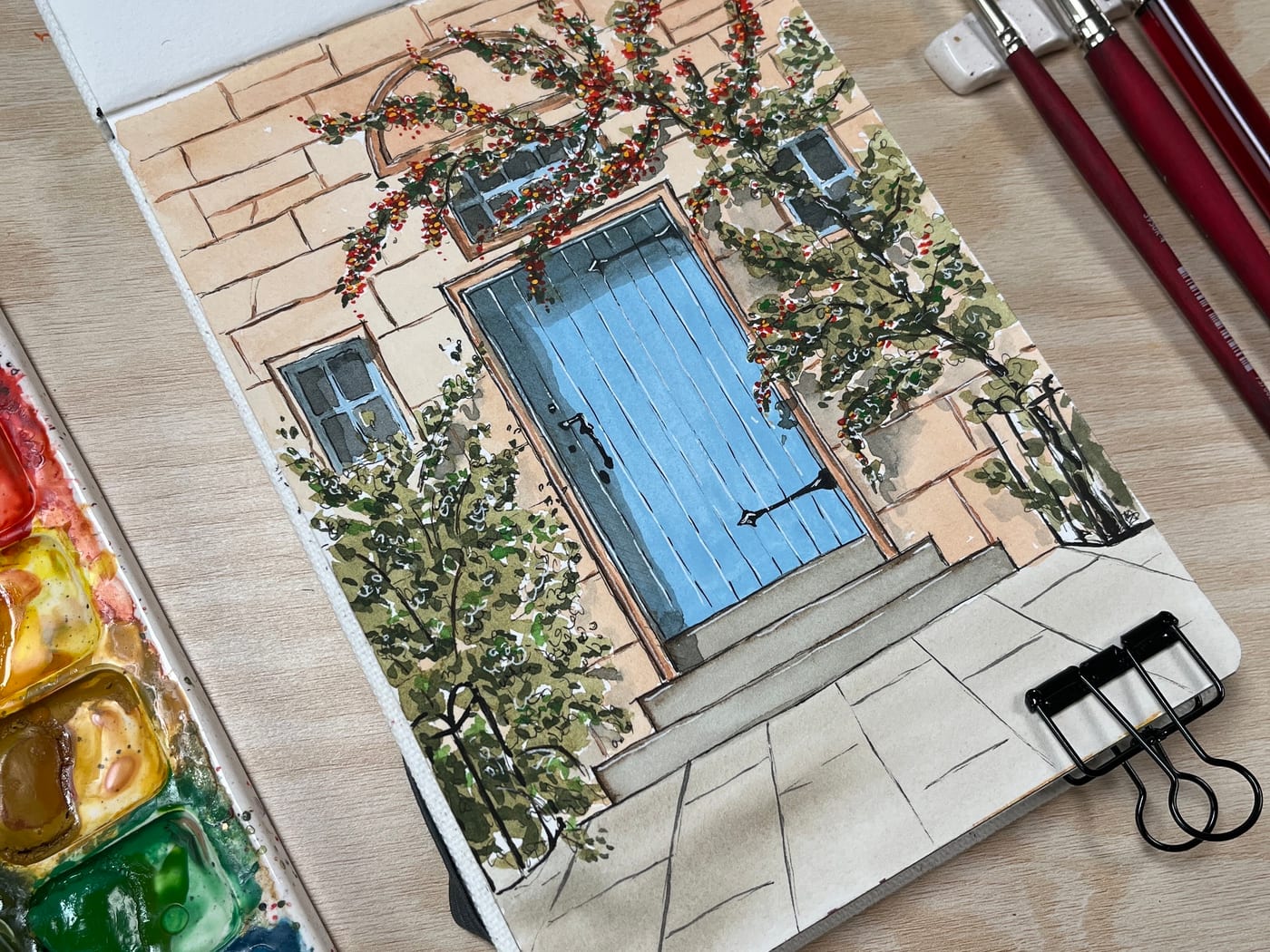 Ink and watercolour sketch of a blue cottage door with a climbing rose