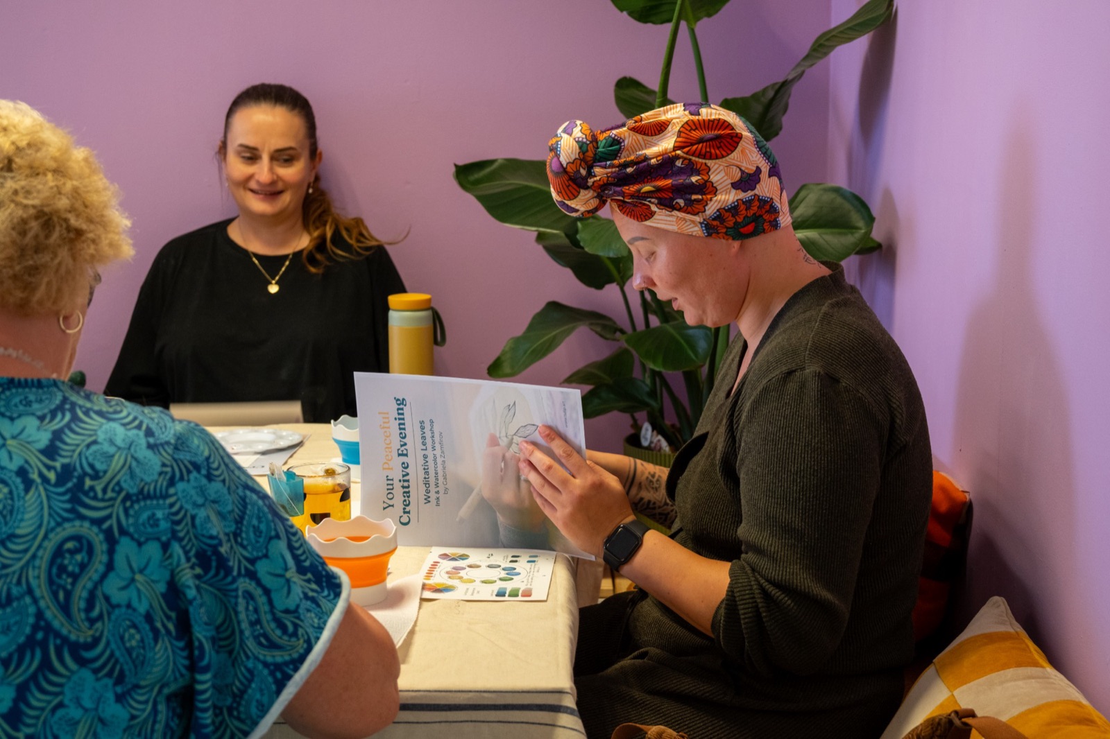 Women at a workshop table in Delft, one reading the Your Peaceful Creative Evening booklet