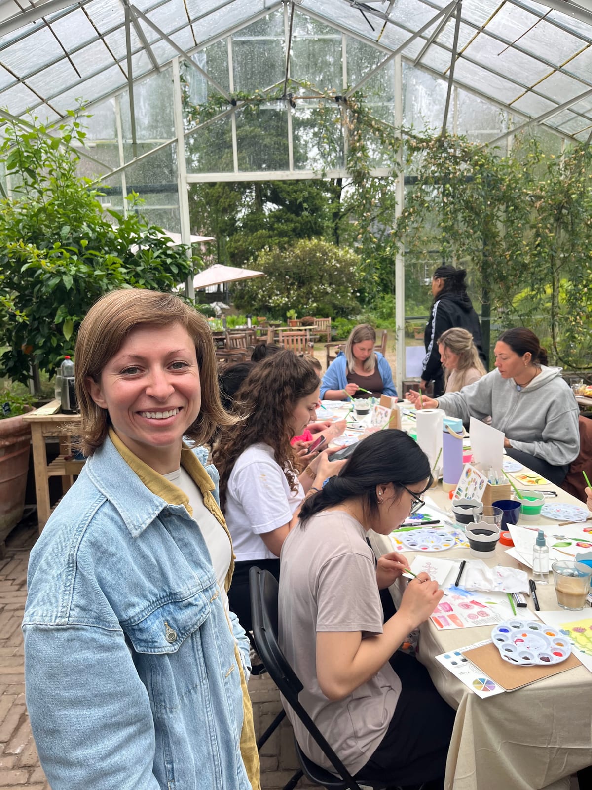 Gabriela smiling in the foreground while a workshop group paints behind her