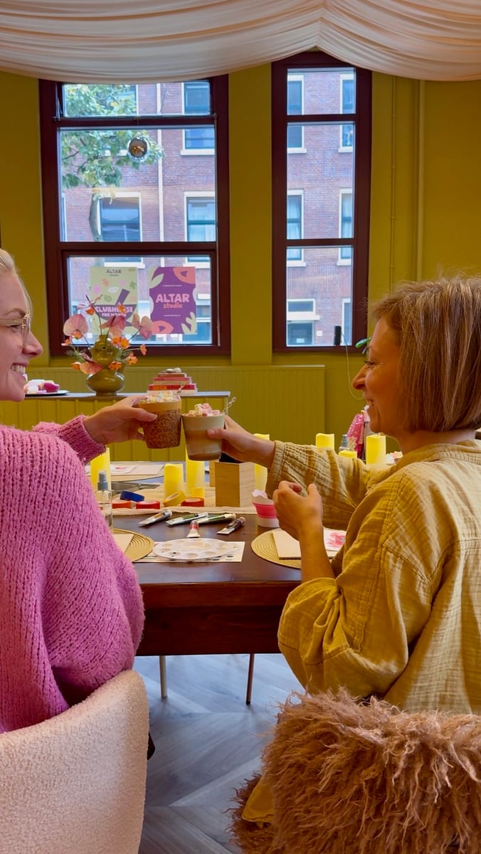 Two women smiling and clinking cups of hot chocolate topped with marshmallows
