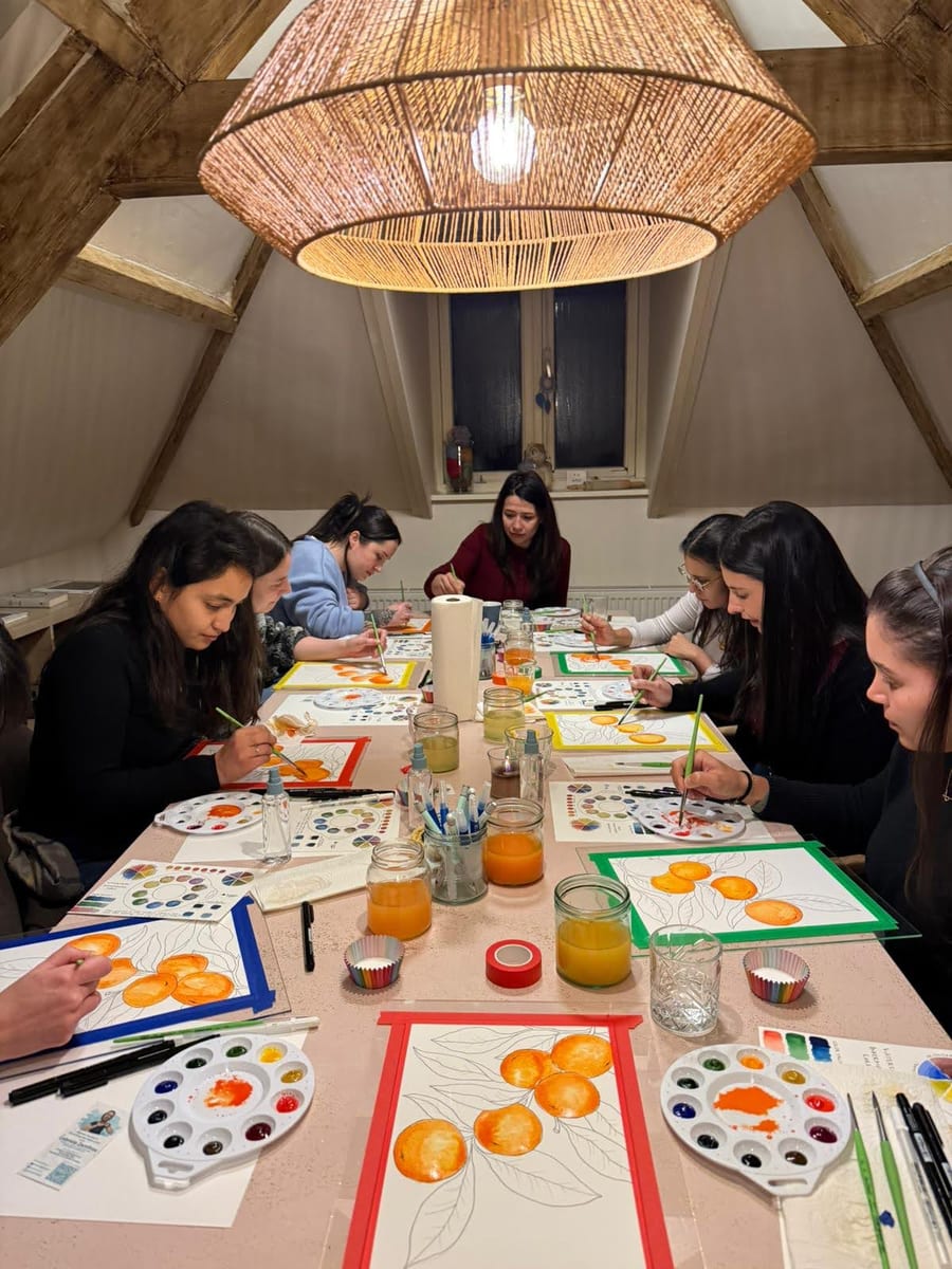 A cosy evening workshop under a rattan lamp, everyone painting bright watercolour oranges