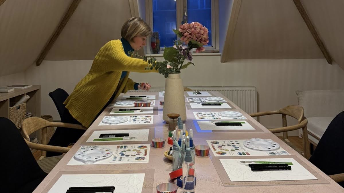 Gabriela arranging flowers on a table set with palettes, brushes and paper for a workshop