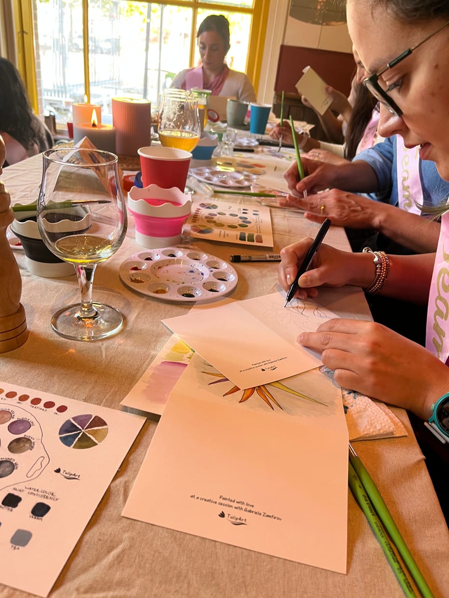 Close up of hands drawing a flower in ink on a card that reads painted with love